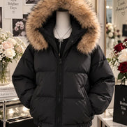 A black puffer jacket with a large tan faux-fur trimmed hood, displayed on a mannequin in a boutique setting.