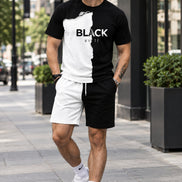 A man wearing a black and white graphic t-shirt with a torn-paper effect and the words 'BLACK WHITE' printed across the chest, paired with white shorts, 