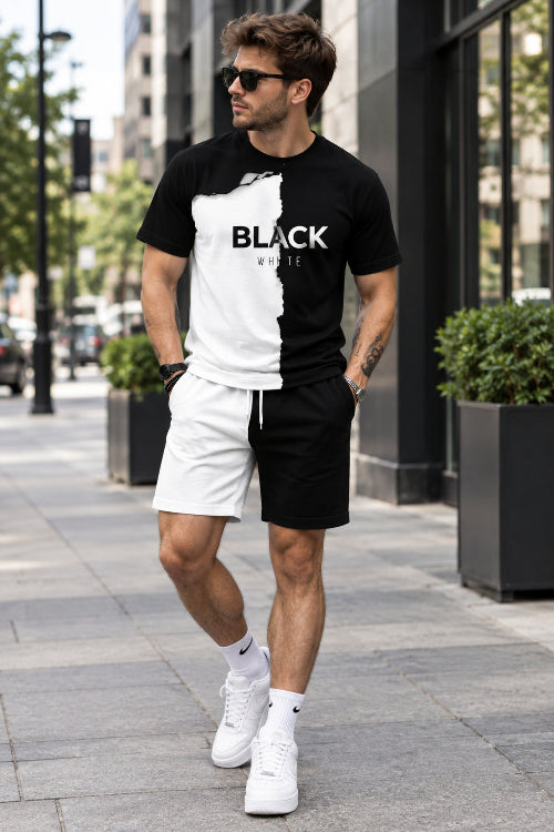 A man wearing a black and white graphic t-shirt with a torn-paper effect and the words 'BLACK WHITE' printed across the chest, paired with white shorts, 