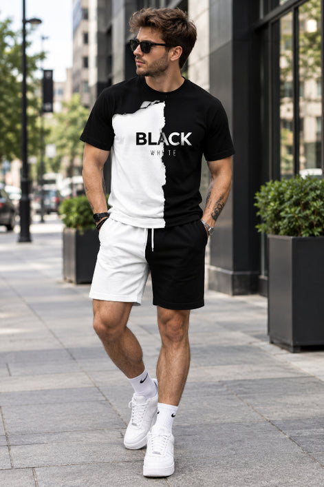 A man wearing a black and white graphic t-shirt with a torn-paper effect and the words 'BLACK WHITE' printed across the chest, paired with white shorts, 