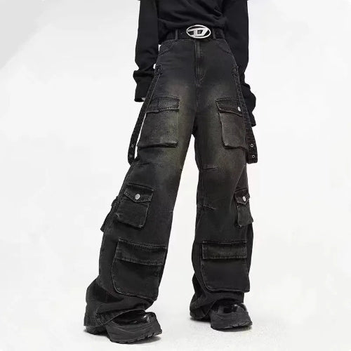 Front view of a model wearing washed black baggy cargo jeans with multiple flap pockets and hanging side straps, paired with black chunky shoes.