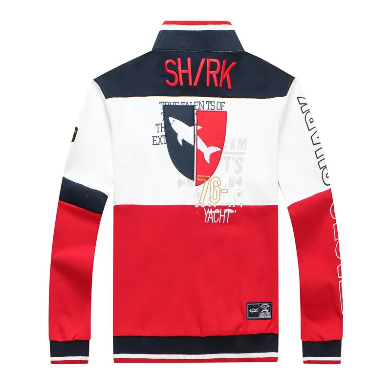 A color-blocked long-sleeve track jacket shown from the back, featuring navy blue, white, and red panels with a shark graphic crest, 'SHARK' text, and sleeve graphics, on a plain white background.