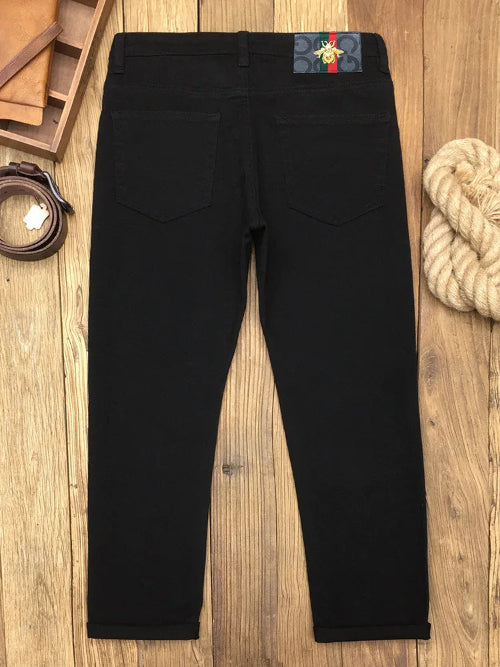 Black slim-fit jeans shown from the back, laid flat on a wooden surface with a belt, leather pieces, and rope as styled props.