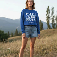 Blue sweatshirt with 'Faith Over Fear' text on a wooden background