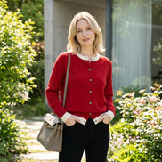 Person wearing a red cardigan with white trim, holding a beige handbag indoors.