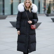 A person taking a mirror selfie wearing a long black puffer coat with a large fluffy light gray fur collar. 