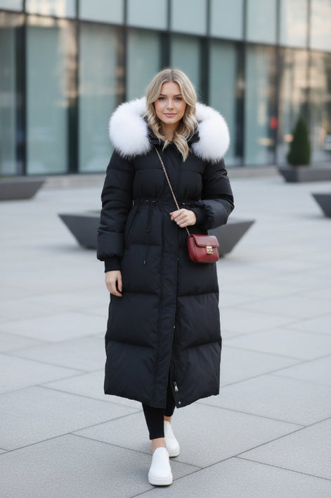 A person taking a mirror selfie wearing a long black puffer coat with a large fluffy light gray fur collar. 