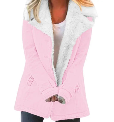 Woman wearing a pink coat with wide white fleece-look lapels, front pockets and cuff tabs over a white top and dark trousers