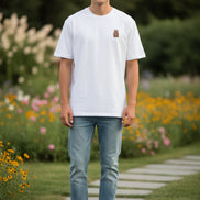White t-shirt with a small brown and gold design on a hanger against a white background