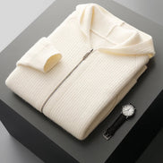 Folded cream-colored sweater on a dark surface with a watch and yellow object.