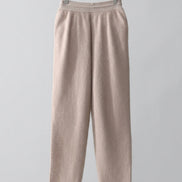 A pair of soft, light beige knit pants hanging on a wooden hanger inside a wooden wardrobe or closet with white drawers.