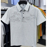 A light gray short-sleeve polo shirt with a subtle tonal landscape graphic across the chest, displayed on a black hanger in a retail setting.