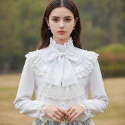 White blouse with lace details and a large bow on a mannequin against a gray background