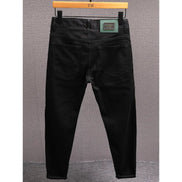 Black slim-fit jeans shown from the back, hanging on a wooden hanger against a textured gray wall.