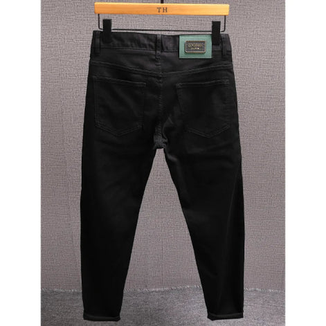 Black slim-fit jeans shown from the back, hanging on a wooden hanger against a textured gray wall.