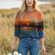 A woman wearing a long-sleeve crewneck sweatshirt with a scenic sunset landscape print, paired with blue jeans and holding a small bouquet of white roses.
