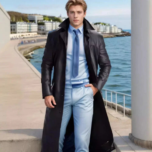 Man in a black coat and light blue suit standing by a waterfront.