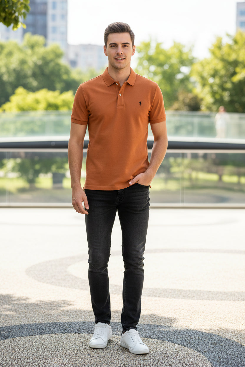Orange polo shirt with a brand logo held by a hand, with other shirts in the background.