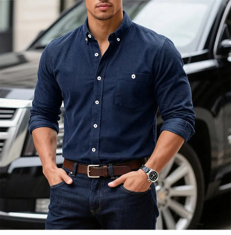 A man wearing a dark navy blue long-sleeve button-down shirt with white buttons, paired with dark jeans and a 