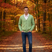 Green cardigan over a white shirt on a wooden hanger against a dark wall.