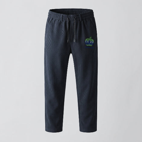 Dark gray pants with a green logo on a hanger against a gray background