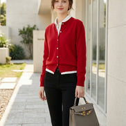 A person wearing a bright red button-front cardigan with white ribbed trim, paired with black pants and carrying a structured light gray handbag