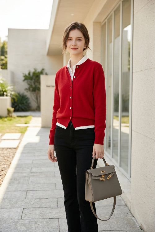 A person wearing a bright red button-front cardigan with white ribbed trim, paired with black pants and carrying a structured light gray handbag