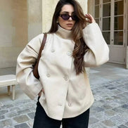 Woman wearing a cream stand-collar double-breasted coat in a stone courtyard