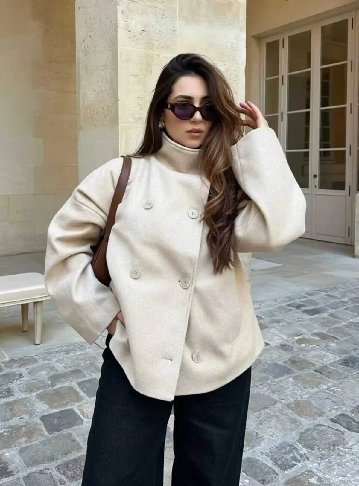 Woman wearing a cream stand-collar double-breasted coat in a stone courtyard