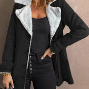 Woman wearing a black jacket with white fleece-look lining, wide lapels and buckled cuffs over a black top and jeans