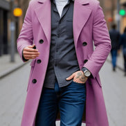 A man wearing a mid-length lavender double-breasted overcoat over a dark gray shirt and blue jeans, walking on a city street.