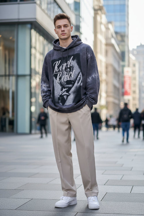 Person wearing a dark hoodie, light pants, and white sneakers in a minimal indoor setting.