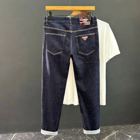 Dark blue denim jeans shown from the back, hanging on a black hanger against a dark gray wall, with a white T-shirt 