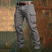 Gray cargo pants with flap thigh pockets and a brown belt against a textured rust-colored metal background.