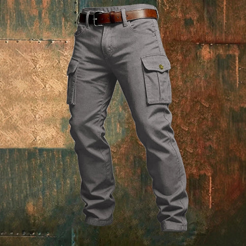 Gray cargo pants with flap thigh pockets and a brown belt against a textured rust-colored metal background.