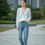A person wearing a soft white fuzzy V-neck cardigan over a ribbed light gray top, with blue jeans