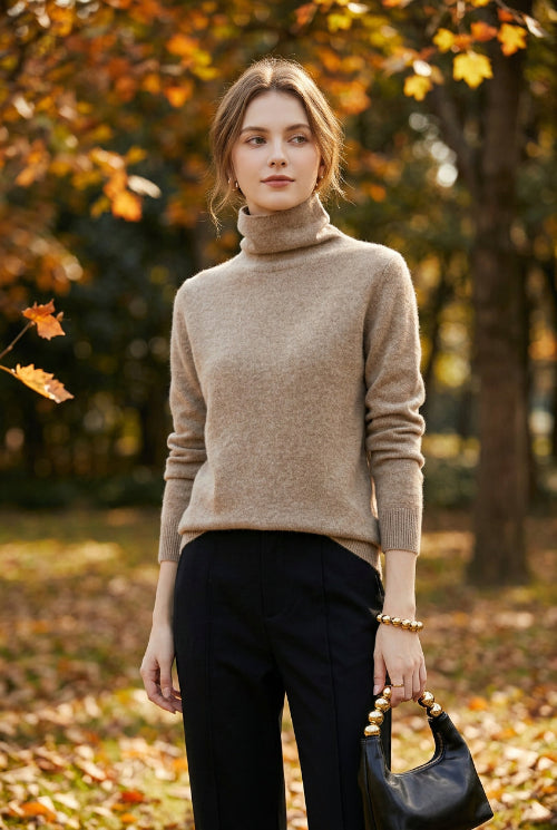 A person wearing a fuzzy light taupe-beige turtleneck sweater, paired with black bottoms and holding a black handbag with gold-tone hardware.