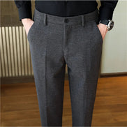 A person wearing dark gray textured trousers with a black shirt, standing indoors with hands in pockets.