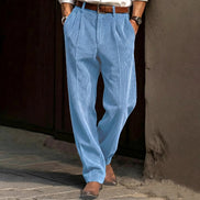 Person wearing light blue pleated pants standing against a dark wall.