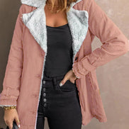 Woman wearing a pink jacket with white fleece-look lining, wide lapels and buckled cuffs over a black top and jeans