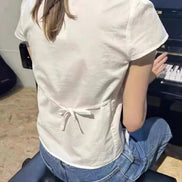 Person playing a piano from behind, wearing a white shirt and blue jeans.