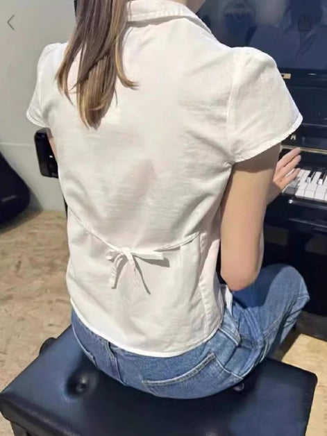Person playing a piano from behind, wearing a white shirt and blue jeans.