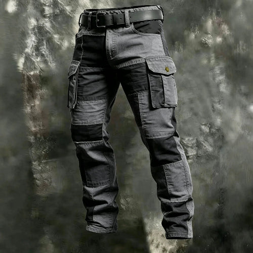 Olive green and black color-block cargo pants with flap thigh pockets and a black belt against a textured gray background.