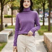 A woman wearing a fuzzy purple turtleneck sweater, paired with light beige pants and a black belt with a gold buckle, shown in a close-up shot.