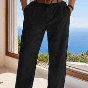 Person wearing black pants with a white shirt and brown belt, standing by a window with a scenic view.