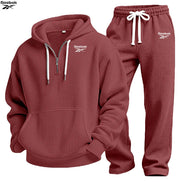 A Reebok two-piece tracksuit set in a dusty rose/mauve waffle fabric, featuring a pullover hoodie with a half-zip neckline and matching jogger pants 