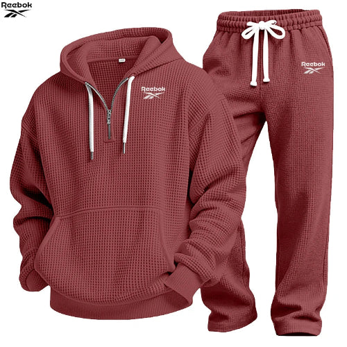 A Reebok two-piece tracksuit set in a dusty rose/mauve waffle fabric, featuring a pullover hoodie with a half-zip neckline and matching jogger pants 