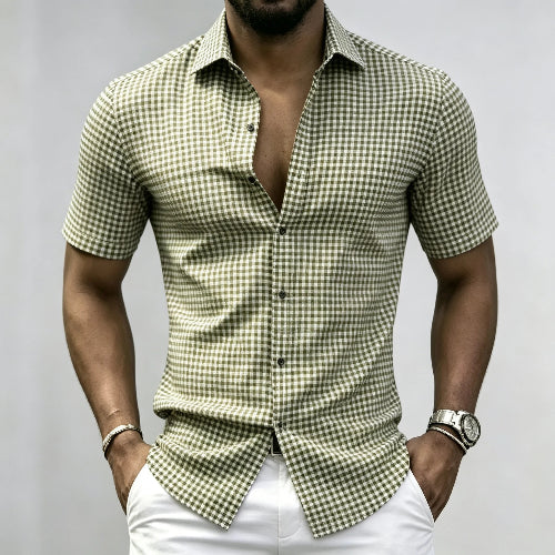 A man wearing a short-sleeve button-up shirt with a green and beige gingham check pattern, paired with white pants, shown from the chin down against a plain light gray background.