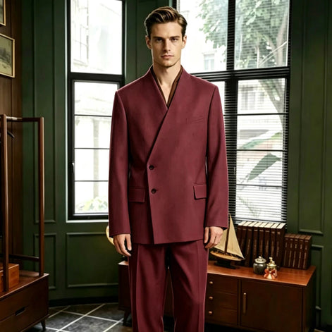 A man wearing a dark burgundy double-breasted suit with a shawl collar, standing in a vintage room with dark green walls and large windows.