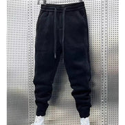 Black baggy sweatpants hanging on a hanger with white sneakers below and a white border around the photo.